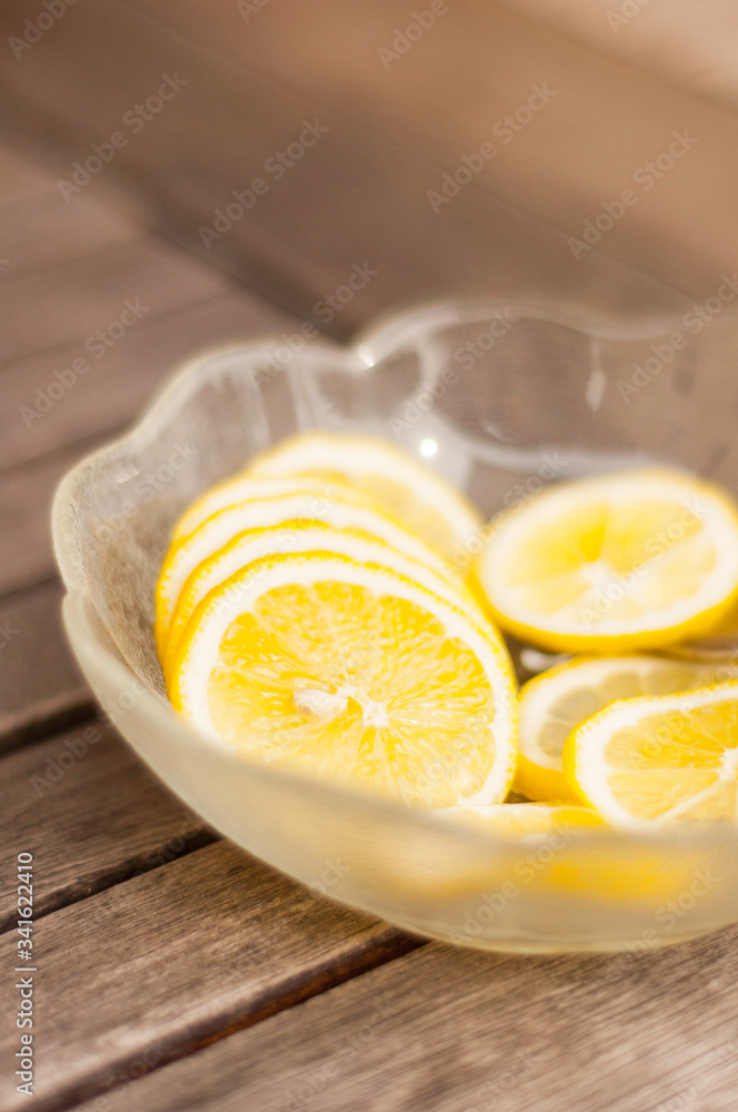 A glass bowl filled with lemon wedges stands on a wooden table. With the spoon, the slices are placed in refreshing water or lemonade. A glass bowl filled with lemon wedges stands on a wooden table. With the spoon, the slices are placed in refreshing water or lemonade.