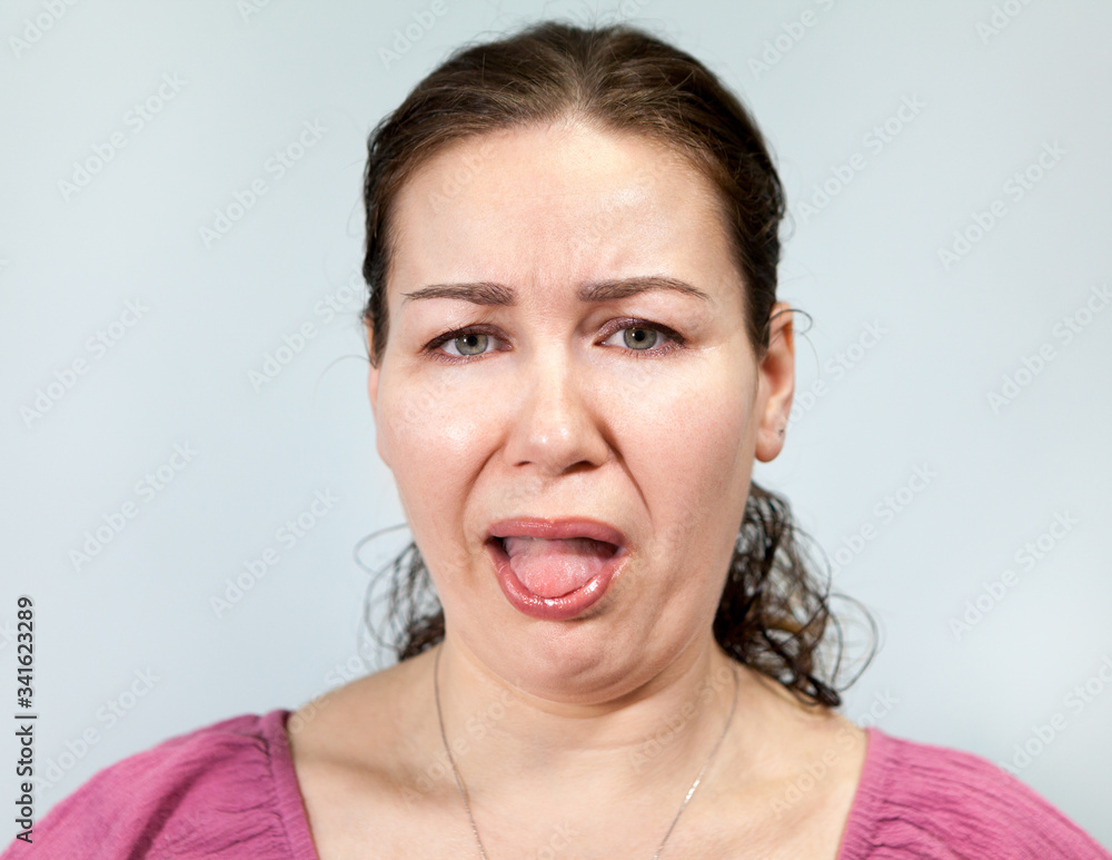 Disgust on a woman's face, open mouth and sticking tongue, portrait on grey background, emotions series Disgust on a woman's face, open mouth and sticking tongue, portrait on grey background, emotions series