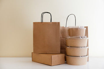 Bunch of blank disposable containers for takeout food stacked with paper bags and boxes with copy space for brand's logo. Close up shot of eco friendly to go carton bowls on table.