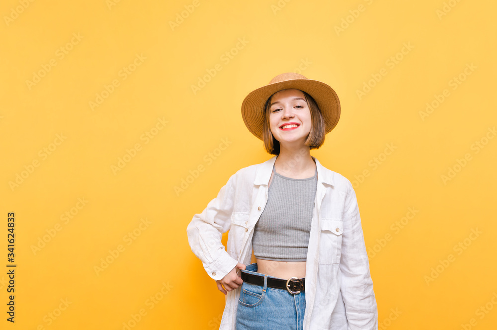 Happy skinny girl in hat and summer clothes isolated on yellow background, looks into the camera with a smile on her face and shows the result of training. A smiling lady shows a large pants size. Happy skinny girl in hat and summer clothes isolated on yellow background, looks into the camera with a smile on her face and shows the result of training. A smiling lady shows a large pants size.