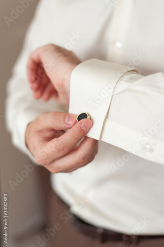 Men's hands adjust cufflinks on the sleeves.
