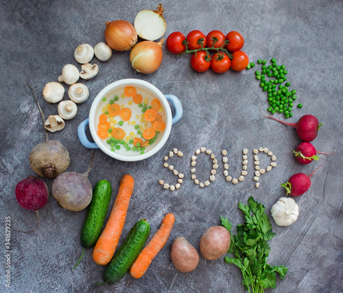 Composition with fresh vegetables on grey background, space for text. Pot with vegetables and word "soup" made of chickpea