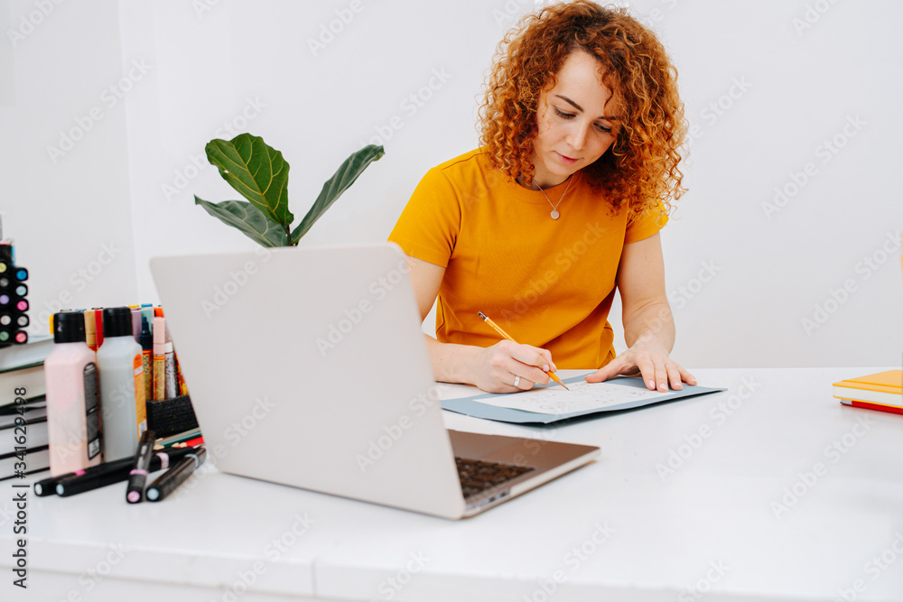 Serious artist woman drawing behind work desk, rushing it to catch up Serious artist woman drawing behind work desk, rushing it to catch up
