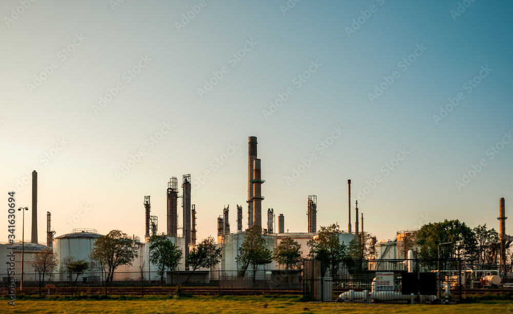 Fototapeta premium Krajobraz przemysłowy, budynek fabryczny w Holandii. Przemysł ciężki w Europie, elektrownia petrochemiczna o zachodzie słońca, zanieczyszczenie kominami, problemy ekologiczne.