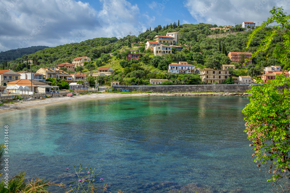 Beautiful summer landscape of the resort with turquoise sea water, village with colorful houses and mountains on the horizon and blue sky. Corfu Island, Greece.