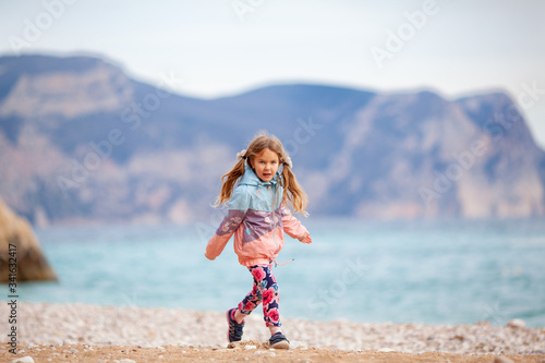 Happy pretty girl walks along the sea coast against the background of the sea, from behind a beautiful landscape