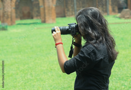 Photography A young girl woman taking photos by DSLR camera keeping her eye in the viewfinder of the camera wearing black shirt