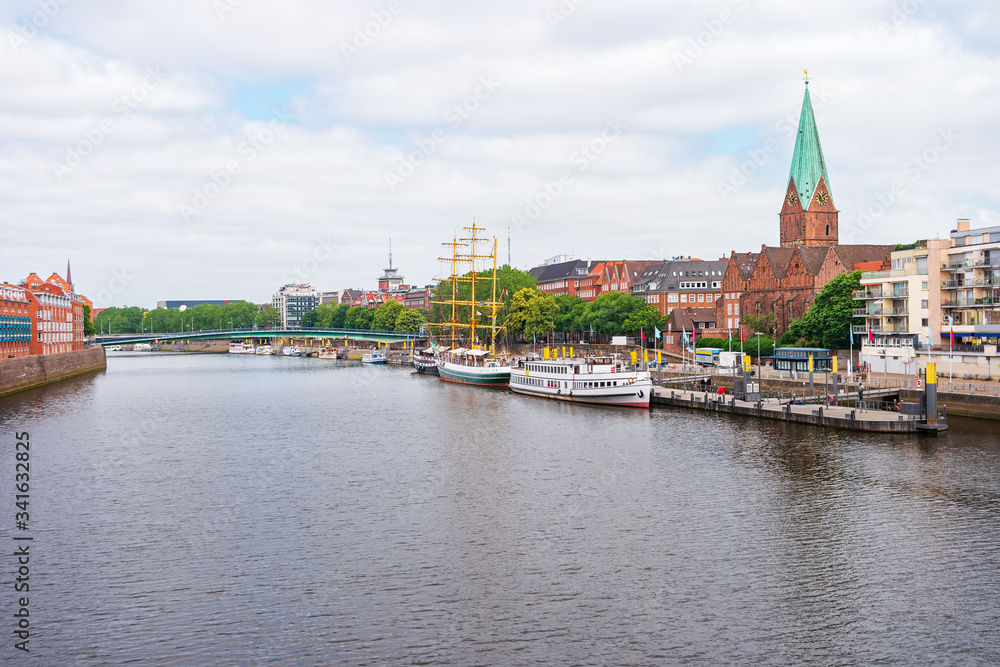 Bremen, Germany. Panoramic city view with a footbridge over the Weser River and the tower of St. Martin's Church. The boats and ships on the pier along the Promenade.