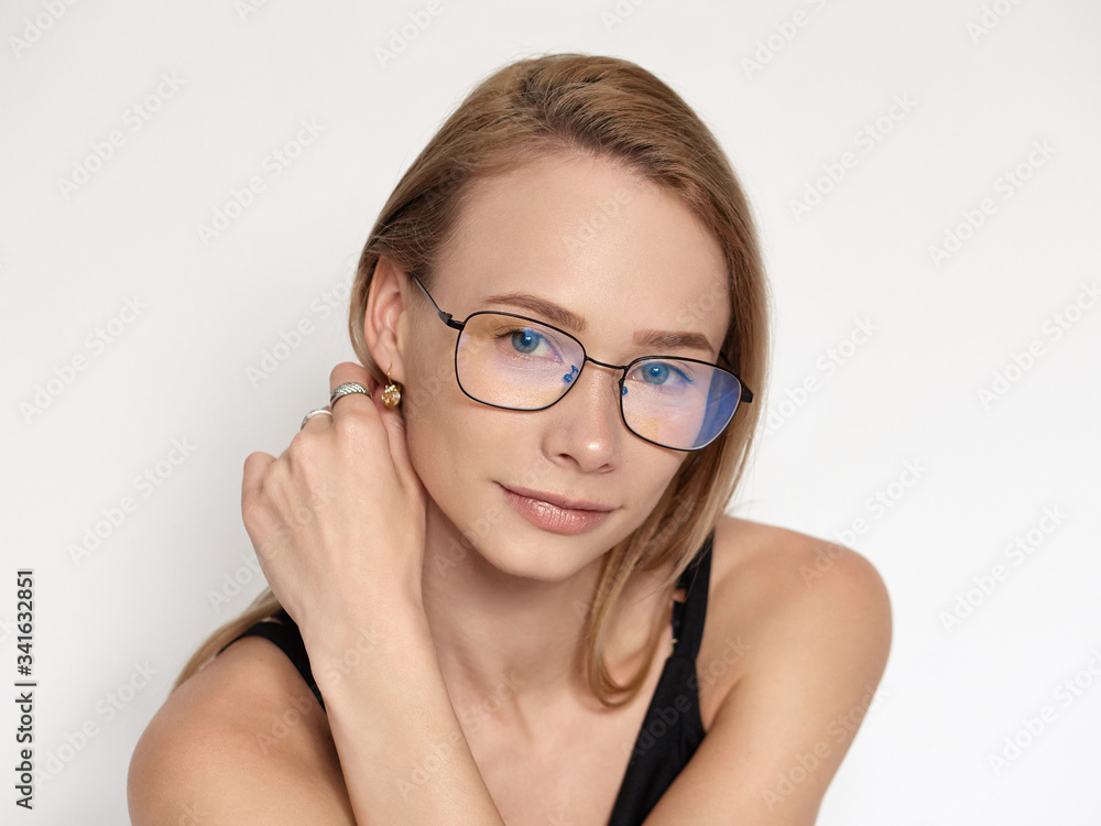 Headshot portrait of a cute natural looking blonde woman wearing simple black blouse and nerd glasses posing on a white background touching her ear Headshot portrait of a cute natural looking blonde woman wearing simple black blouse and nerd glasses posing on a white background touching her ear