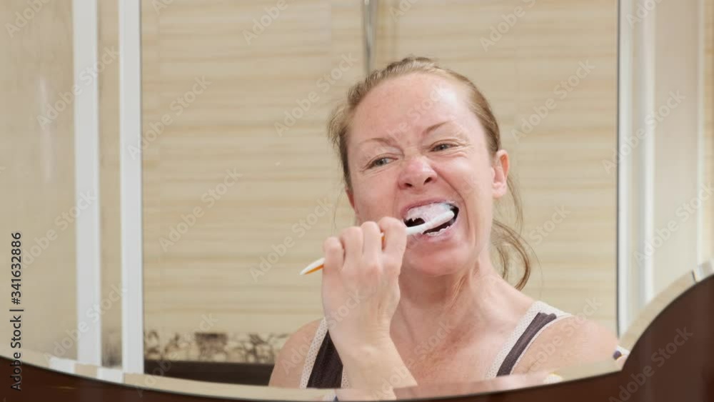 Portrait adult woman brushes teeth looking in mirror in bathroom. Portrait adult woman brushes teeth looking in mirror in bathroom.