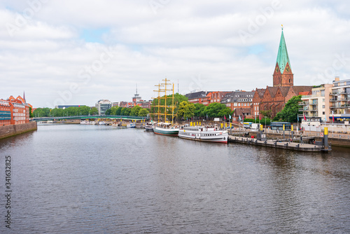 Bremen, Germany. Panoramic city view with a footbridge over the Weser River and the tower of St. Martin's Church. The boats and ships on the pier along the Promenade.