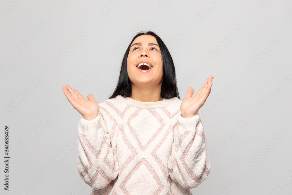 Portrait of a beautiful woman in a warm winter sweater smiles and spreads her arms to the sides, standing on a gray background and looking at the camera Portrait of a beautiful woman in a warm winter sweater smiles and spreads her arms to the sides, standing on a gray background and looking at the camera