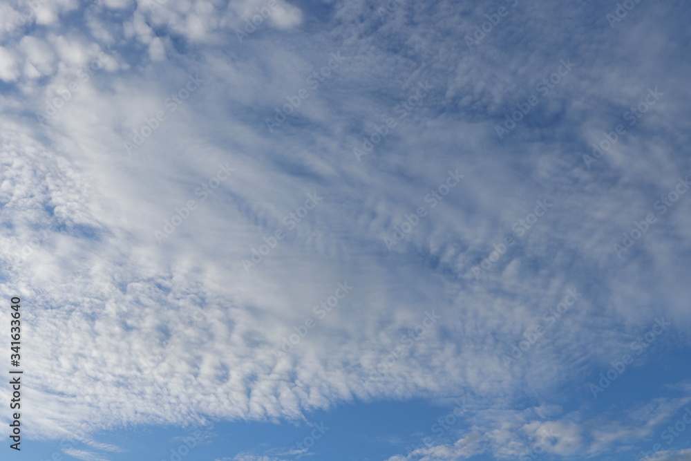 White altocumulus clouds and blue sky background.