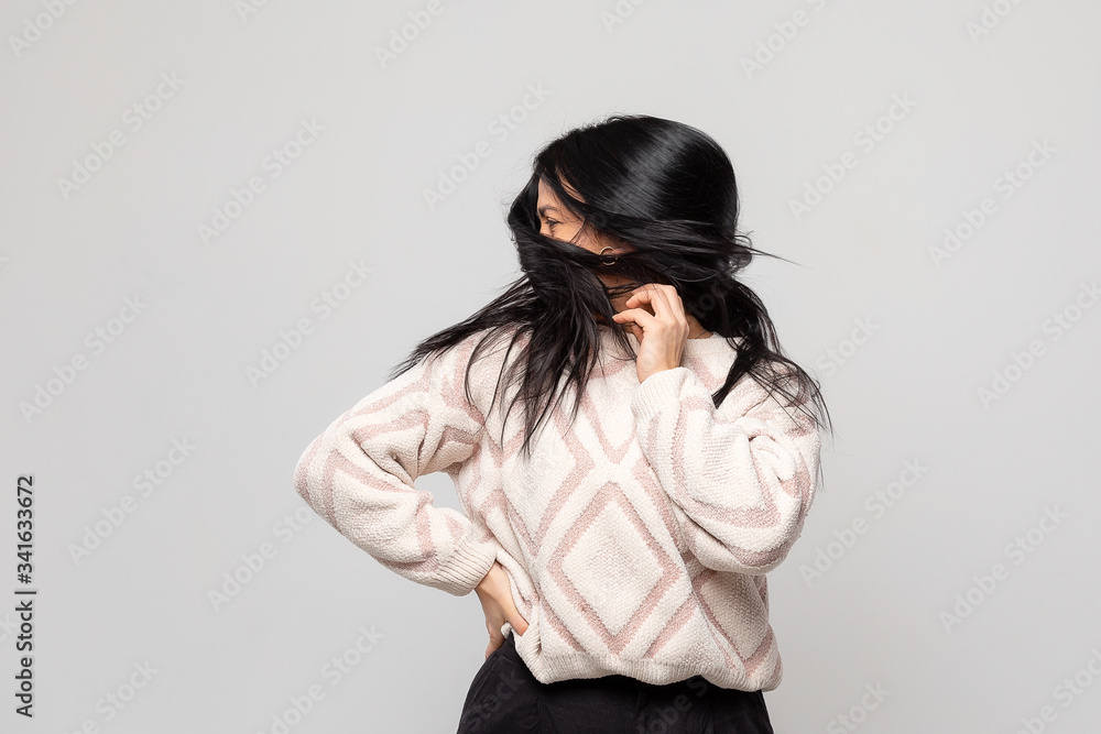Portrait of a young woman with long messed-up hair covering her face isolated against a light grey background Portrait of a young woman with long messed-up hair covering her face isolated against a light grey background
