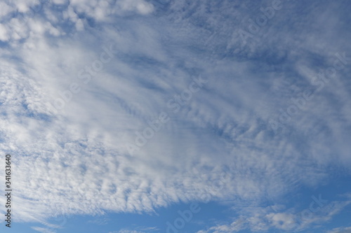 White altocumulus clouds and blue sky background.