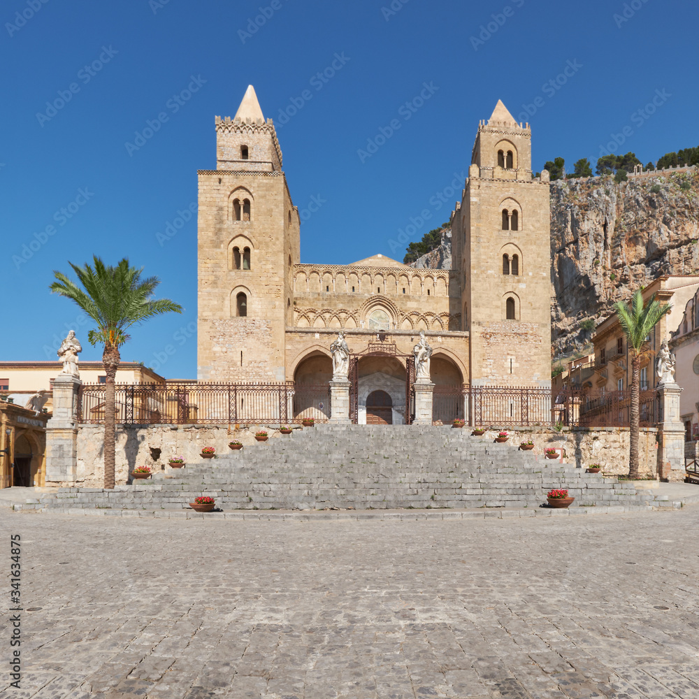 Duomo di Cefalu of the famous unesco heritage church in Cefalu, flowerpots decorate the stairs the famous rock (Rocca di Cefalu) in the background