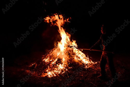 A man throws dry leaves into a large fire, night.