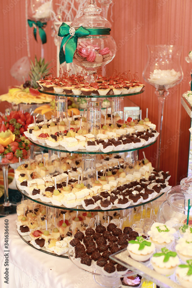 Candy bar. White wedding cake decorated by flowers standing of festive table with deserts, strawberry tartlet and cupcakes. Wedding. Reception Tartlets Candy bar. White wedding cake decorated by flowers standing of festive table with deserts, strawberry tartlet and cupcakes. Wedding. Reception Tartlets