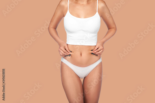 Young, healthy and beautiful blonde woman in white lingerie. Sport, fitness, diet, weight loss and healthcare concept. Slim female belly, girl holding her skin for cellulite check.