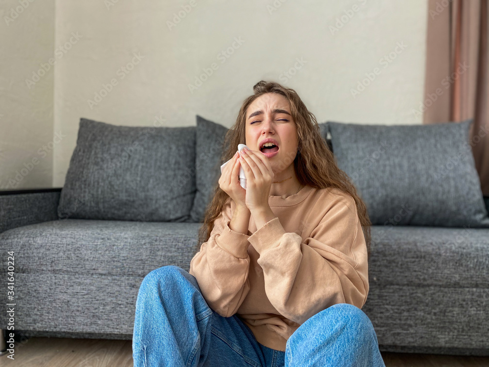 Young woman falls ill, sneezes and takes pills for fever and headache while sitting at home in quarantine during the coronavirus pandemic. Young woman falls ill, sneezes and takes pills for fever and headache while sitting at home in quarantine during the coronavirus pandemic.