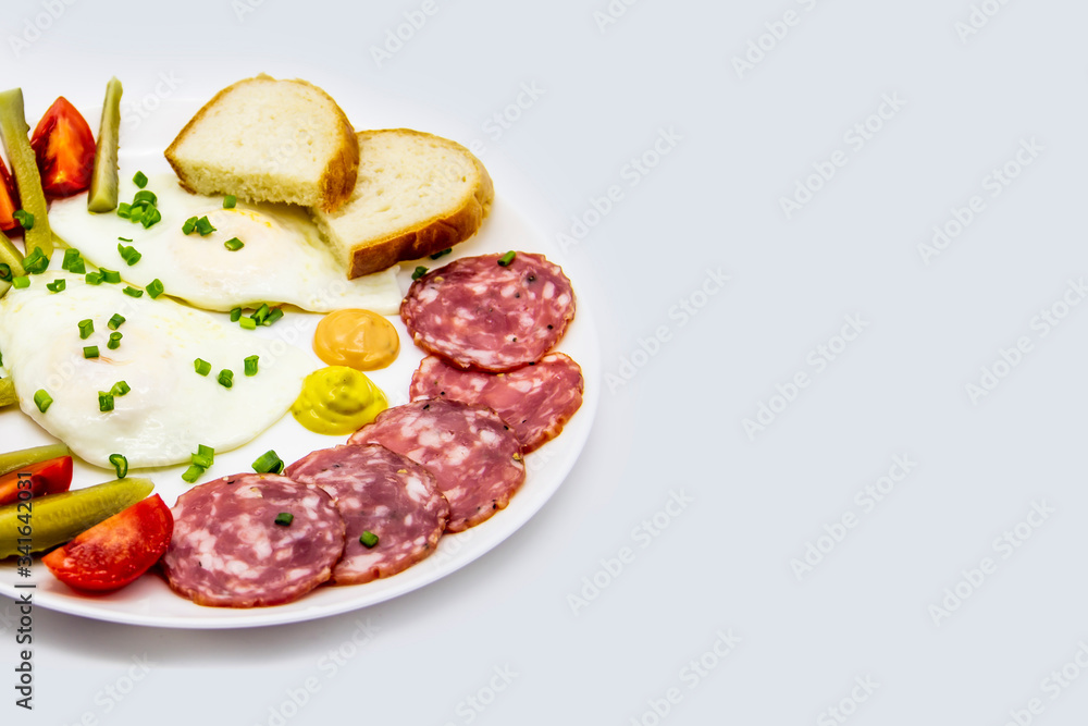 Delicious breakfast with eggs, salami, cucumbers, cherry tomatoes, slices of loaf, sauces and green onion on top on a white plate. Healthy and tasty meal for breakfast or lunch.