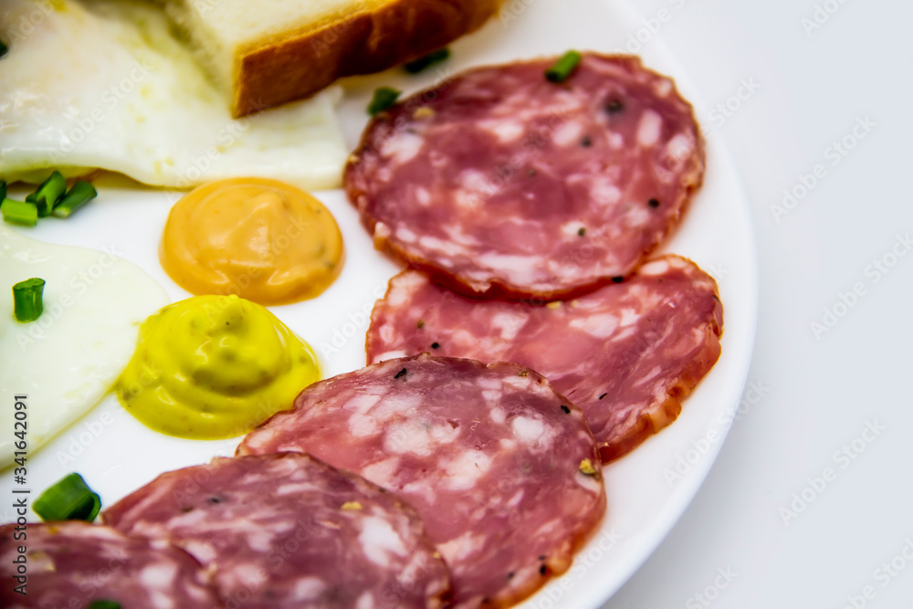 Delicious breakfast with eggs, salami, slices of loaf, sauces and green onion on top on a white plate. Healthy and tasty meal for breakfast or lunch. Delicious breakfast with eggs, salami, slices of loaf, sauces and green onion on top on a white plate. Healthy and tasty meal for breakfast or lunch.