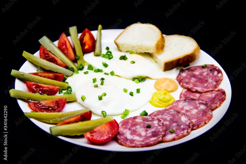 Delicious breakfast with eggs, salami, cucumbers, cherry tomatoes, slices of loaf, sauces and green onion on top on a white plate. Healthy and tasty meal for breakfast or lunch. Delicious breakfast with eggs, salami, cucumbers, cherry tomatoes, slices of loaf, sauces and green onion on top on a white plate. Healthy and tasty meal for breakfast or lunch.
