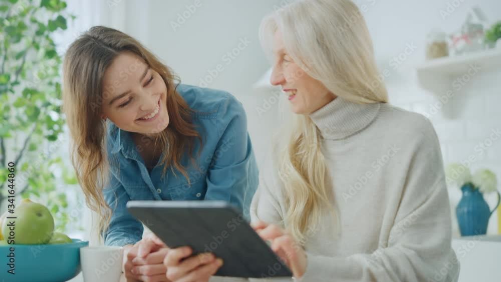 Beautiful Granddaughter Teaches Her Grandmother to Use a Tablet Computer. Authentic Senior Woman Browses Internet and Writes Texts on a Gadget. Family Values in Modern Technological Age. Beautiful Granddaughter Teaches Her Grandmother to Use a Tablet Computer. Authentic Senior Woman Browses Internet and Writes Texts on a Gadget. Family Values in Modern Technological Age.