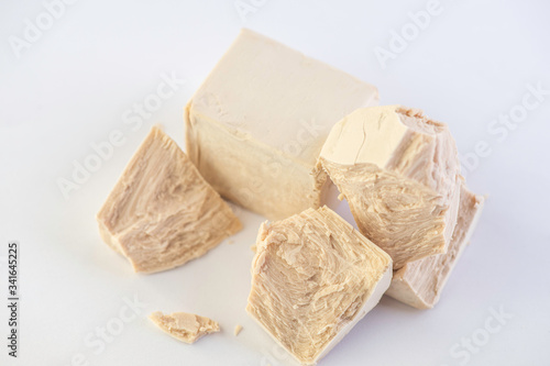 cube of fresh yeast whole and crumbled on a white background 