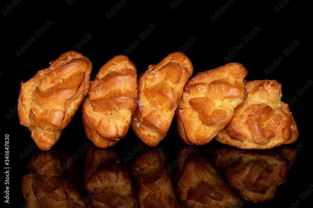 Group of five whole fresh baked profiterole in row isolated on black glass