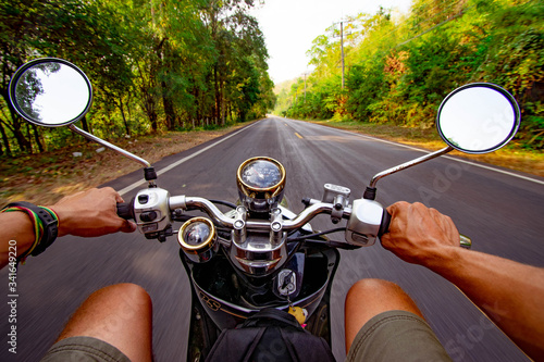 Man on motorcycle driving down an empty road through a forest photo