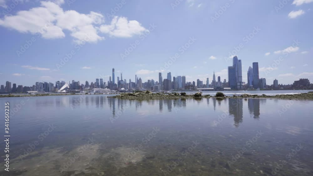 Wide NYC skyline reflecting on shallow Hudson River as camera pushing in over rocks to water Wide NYC skyline reflecting on shallow Hudson River as camera pushing in over rocks to water