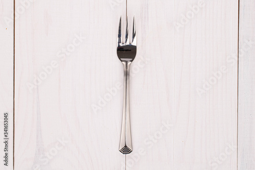 One whole dessert fork on white wood
