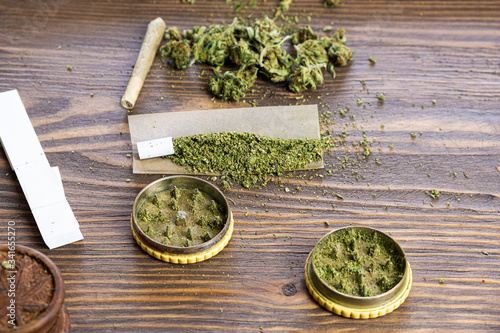 Cannabis joint, marijauna grinder, grinded marijuana, cannabis buds on wooden background