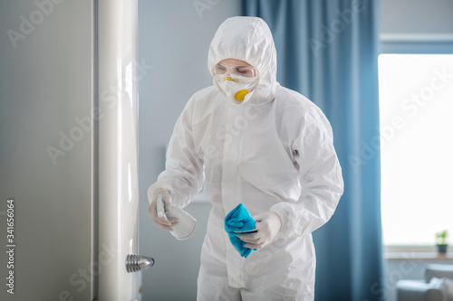 Person in white workwear and gloves disinfecting the surface of the fridge