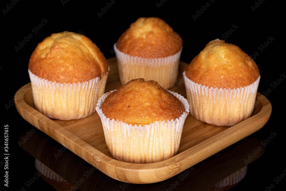 Group of four whole small baked muffin on wooden square plate isolated on black glass Group of four whole small baked muffin on wooden square plate isolated on black glass