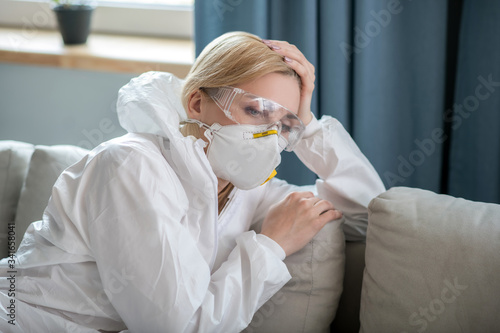 Blonde woman in white workwear and respirator looking tired photo