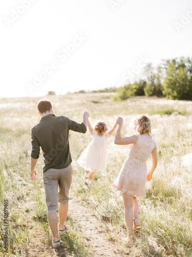 Happy young family of three smiling while spending free time outdoors. Happy loving family walking outdoor in the light of sunset. Father, mother and daughter.