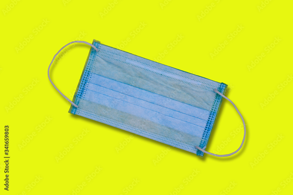 Blue disposable medical mask on a yellow background, close-up with copy space, top view Blue disposable medical mask on a yellow background, close-up with copy space, top view