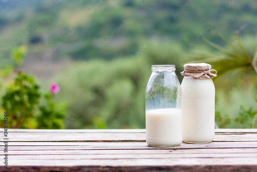 Fresh milk in a bottle standing on a wooden table on the background of nature. Kefir, milk or Turkish Ayran drink in a glass bottle. Space for text Fresh milk in a bottle standing on a wooden table on the background of nature. Kefir, milk or Turkish Ayran drink in a glass bottle. Space for text