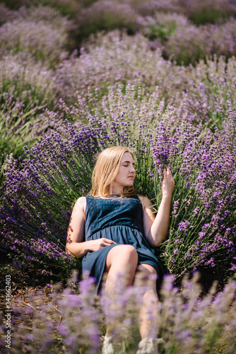 Fototapeta Naklejka Na Ścianę i Meble -  Beautiful girl in dress lying down on purple the lavender field. Beautiful woman in the lavender field on sunset in France. Soft focus. Enjoy on the floral glade, summer nature.