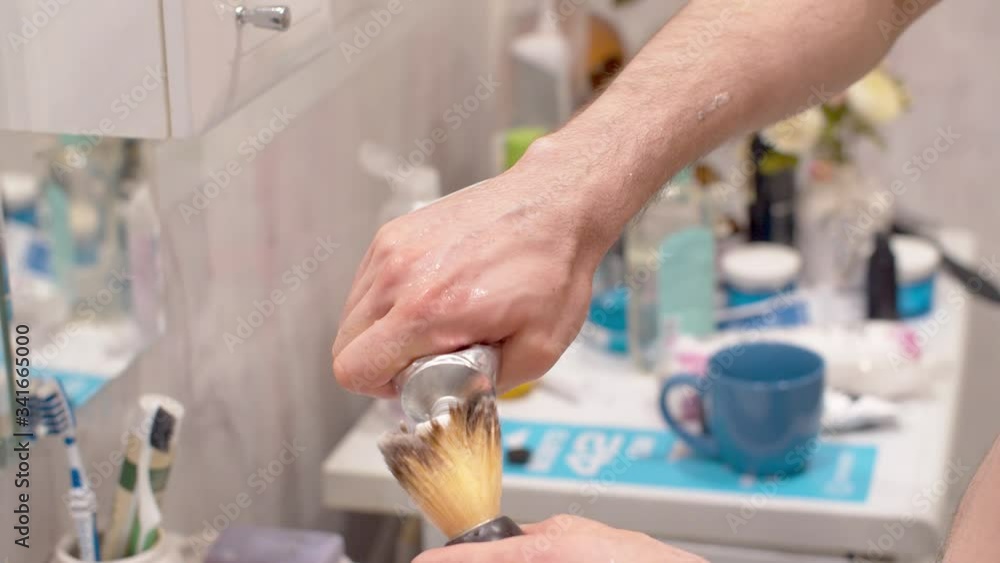 Close-up hands of young man applying shaving foam to a brush. Man shaving in a bathroom. Daily face care Close-up hands of young man applying shaving foam to a brush. Man shaving in a bathroom. Daily face care