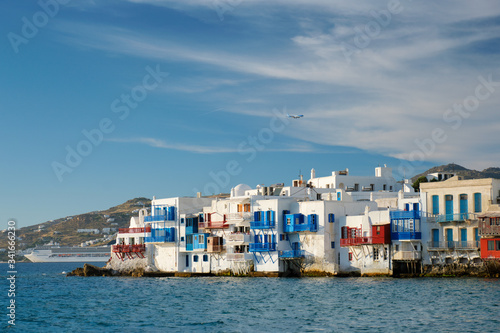 Sunset in Mykonos island, Greece with yachts in the harbor and colorful waterfront houses of Little Venice romantic spot on sunset and cruise ship and plane. Mykonos townd, Greece