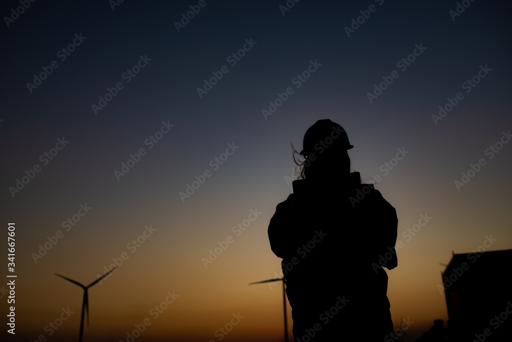 Silhouette of women engineer working and holding the report at wind turbine farm Power Generator Station on mountain,Thailand people Silhouette of women engineer working and holding the report at wind turbine farm Power Generator Station on mountain,Thailand people