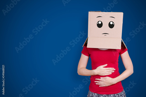 Person with cardboard box on its head and an expectant face expression holding ist belly on dark blue background