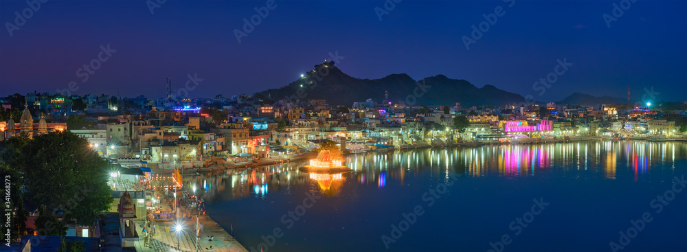 View of famous indian hinduism pilgrimage town sacred holy hindu religious city Pushkar with Brahma temple, aarti ceremony, lake and ghats illuminated at sunset. Rajasthan, India. Horizontal pan