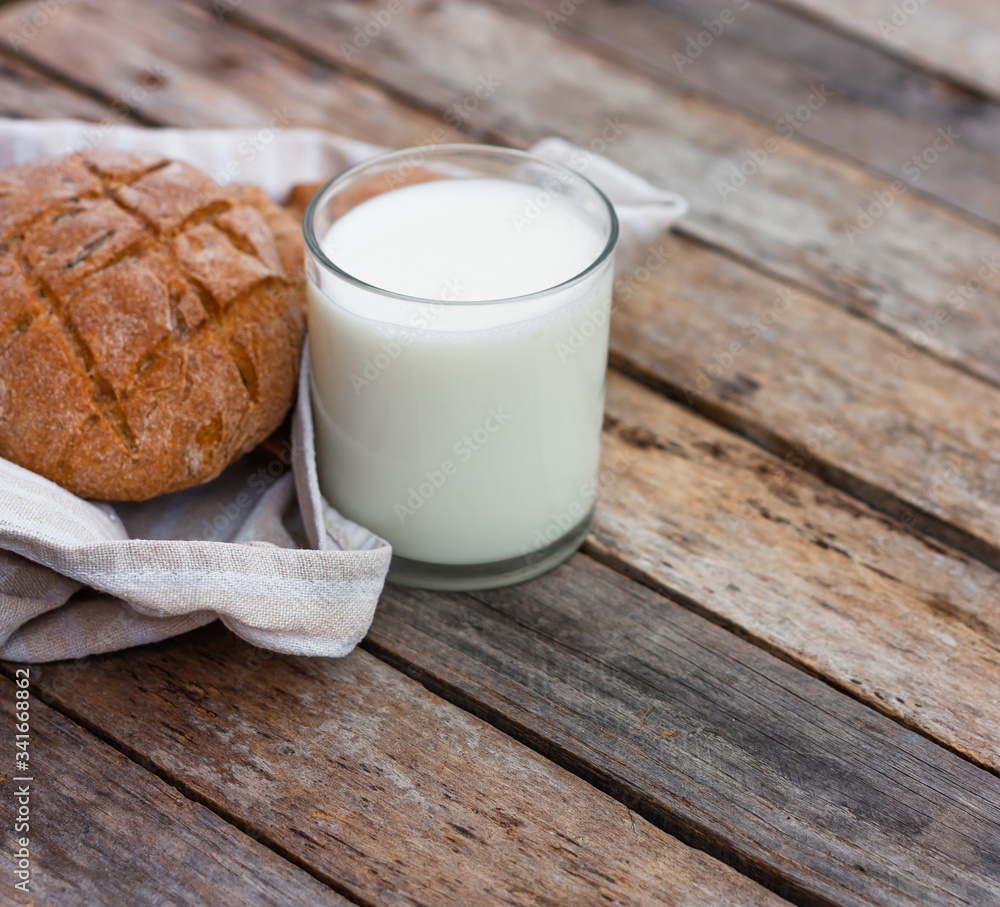 Glass of fresh organic milk and round brown rye fletbread on a rustic wooden table. Kefir, milk or Turkish Ayran drink. Space for text Glass of fresh organic milk and round brown rye fletbread on a rustic wooden table. Kefir, milk or Turkish Ayran drink. Space for text