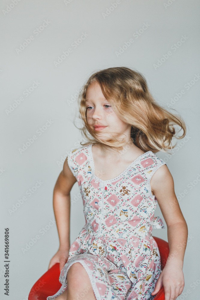 cute European teen girl on a gray background sitting on a red chair. beautiful curly blonde with white teeth. hair cute European teen girl on a gray background sitting on a red chair. beautiful curly blonde with white teeth. hair