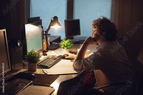 Wallpaper Mural Working with graphs. Man working in office alone during COVID-19 quarantine, staying to late night. Young businessman, manager doing tasks with smartphone, laptop, tablet in empty workspace. Torontodigital.ca