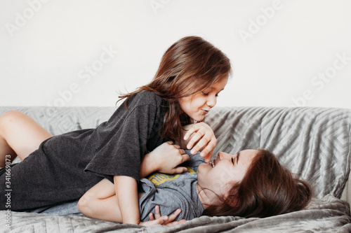 Two little girls, sisters playing at home, jumping on the couch, hugging, kissing each other, fighting, arguing, isolation, vacation, weekend at home, communication